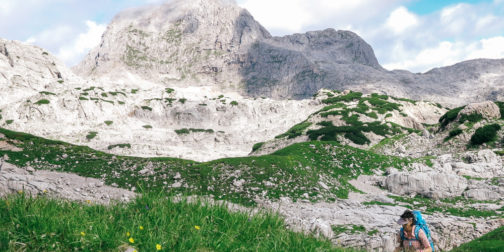 alpine-matten-wandern-großer-Hundstod-Steinernes-Meer Wanderin im Steinernen Meer mit grüner Wiese und grauem Kalkfels im Hintergrund mit Wolken am Himmel