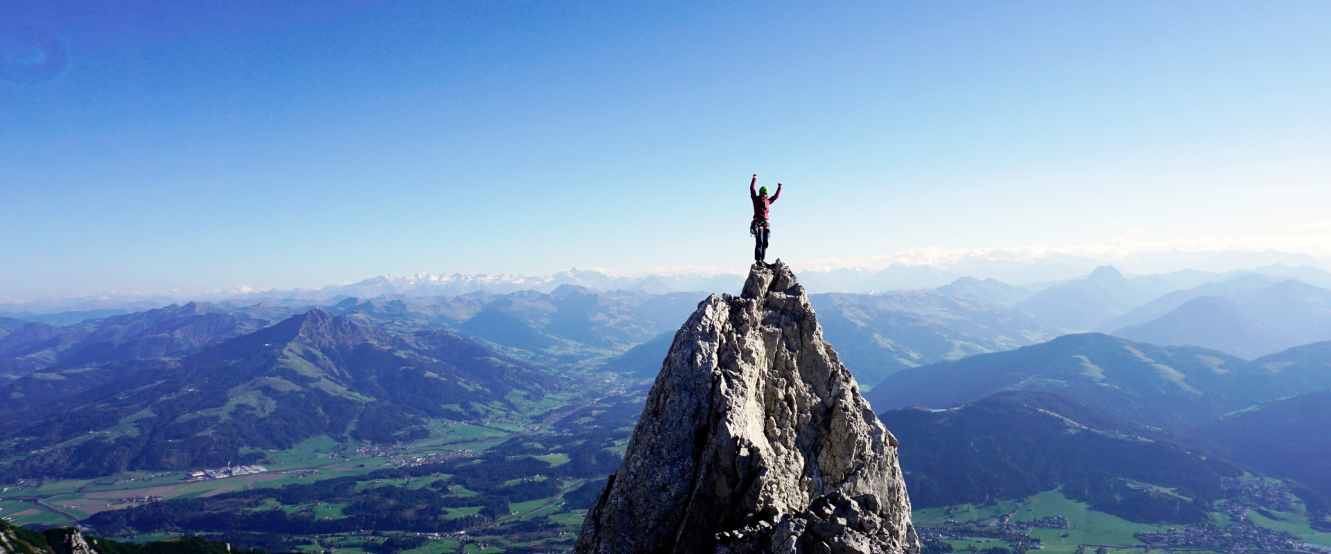 Eva Schider steht auf einem Felszacken im wilden Kaiser mit viel Himmel und Weite im Panorama Hintergrund.