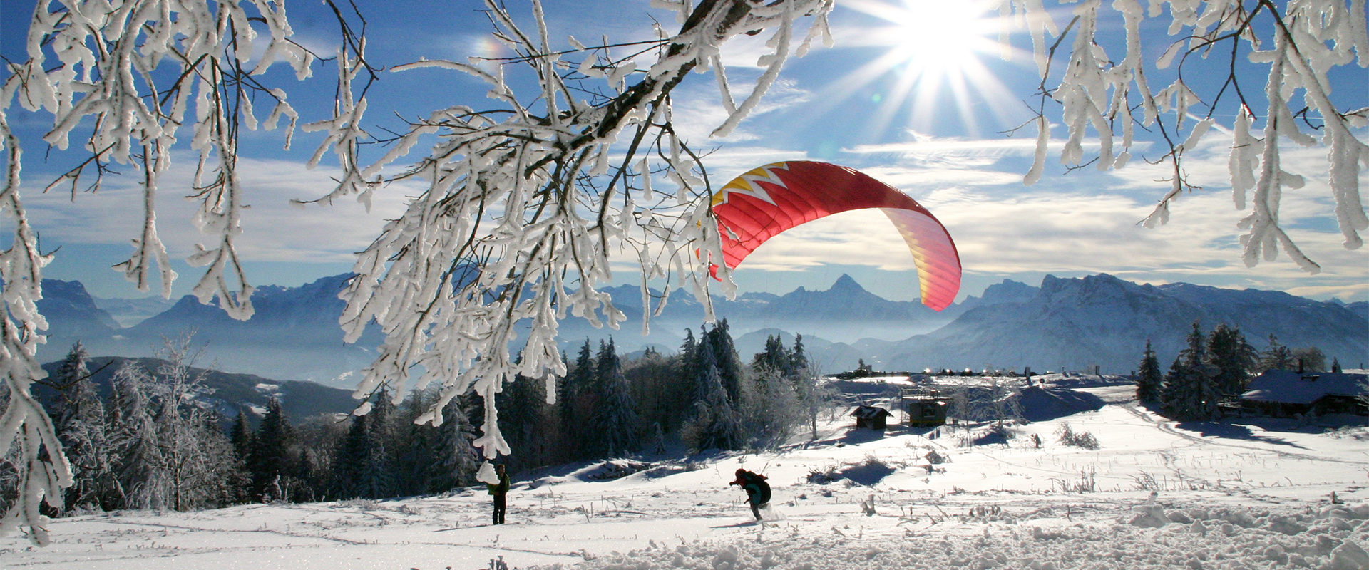 In einer winterlichen Landschaft und bei Sonnenschein wird am Gaisberg ein roter Gleitschirm aufgezogen.