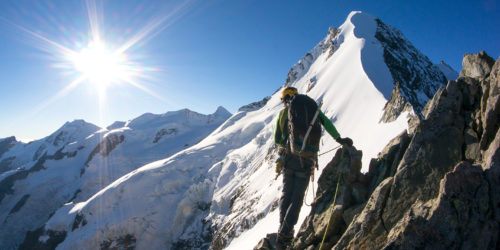 Bergsteiger im Sonnenschein vor schneebedecktem Gipfel