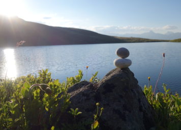 Steinmann übereinander mit Sonne und See in Balance und Ruhe