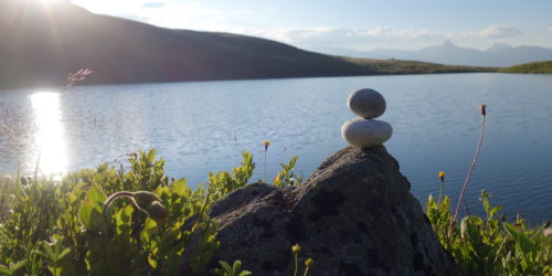 Steinmann übereinander mit Sonne und See in Balance und Ruhe