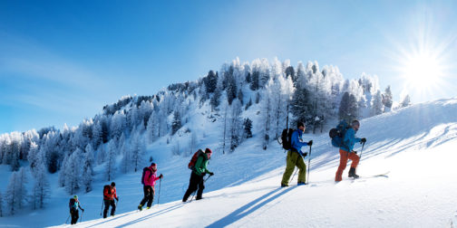 Skitourengruppe im Winter im Aufstieg mit Sonne und glitzerndem Schnee.