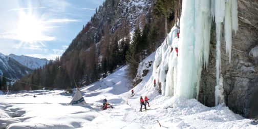 Eiskletterer klettern im Eiskletterpark in Osttirol mit strahlender Sonne und blauen Eisformationen.