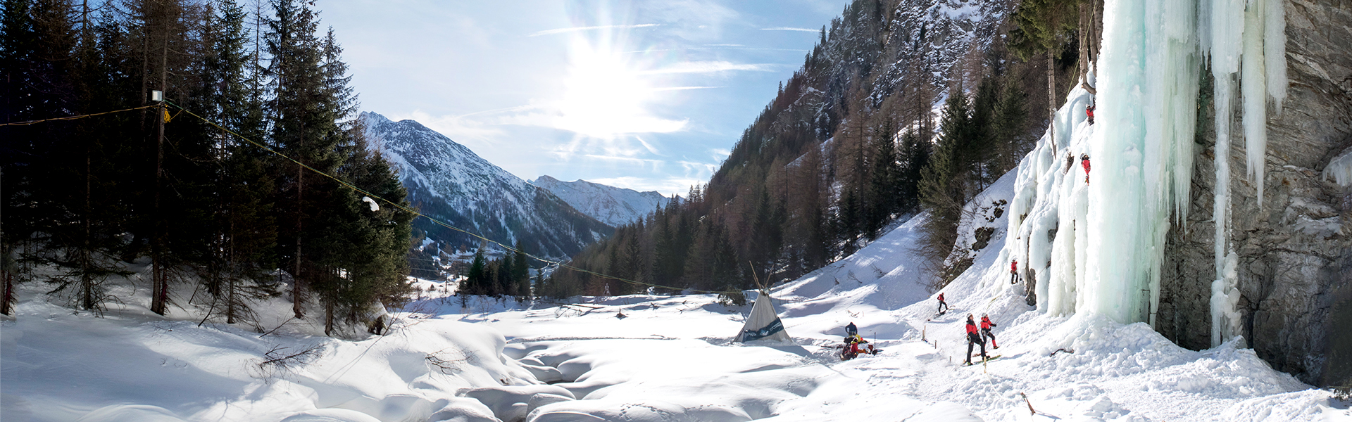 Eiskletterer klettern im Eiskletterpark in Osttirol mit strahlender Sonne und blauen Eisformationen.